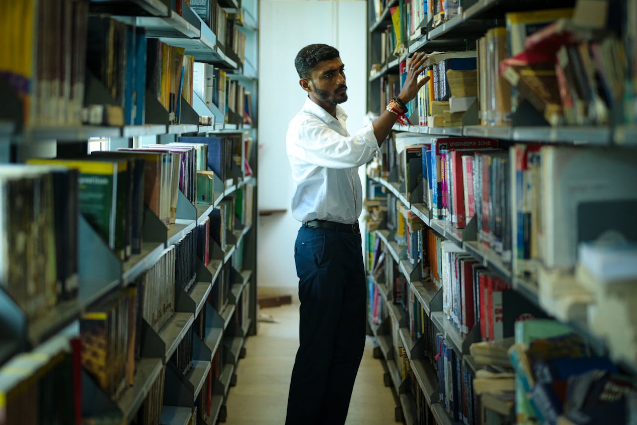 Young Man Browsing Books in a College Library Aisle