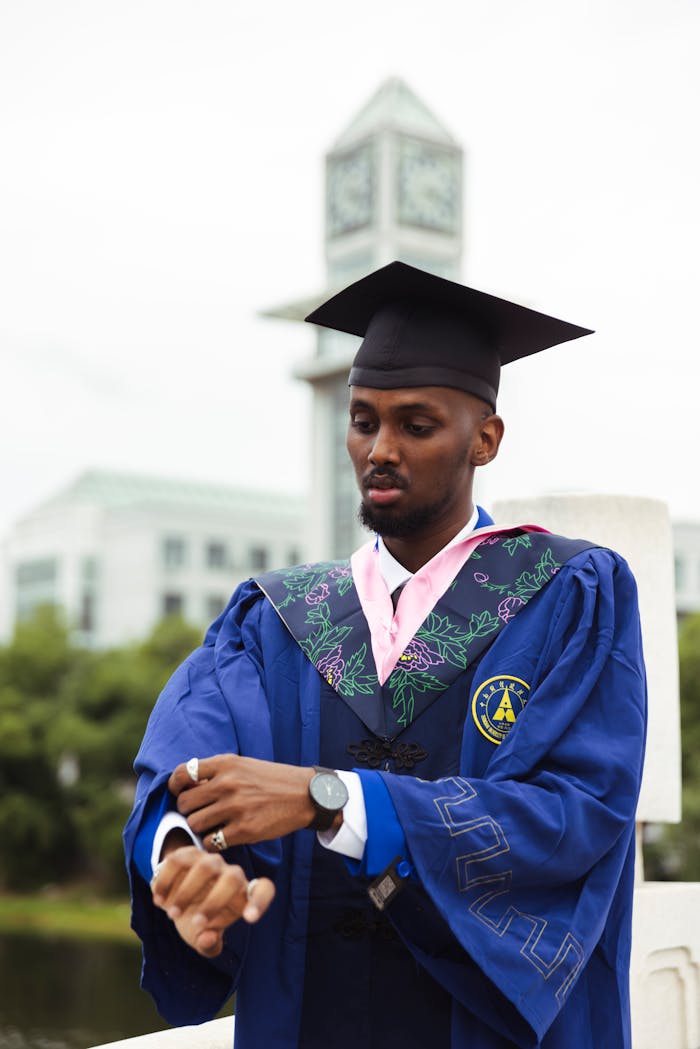 young-graduate-adjusting-sleeve-near-clock-tower-32703400